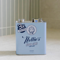 A light blue metal can of Nellie's Floor Care concentrated cleaner, standing on a light countertop with a tiled wall in the background.
