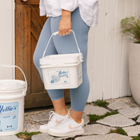 woman carrying a 500 scoop Oxygen Brightener bucket, with other bulk buckets in background.