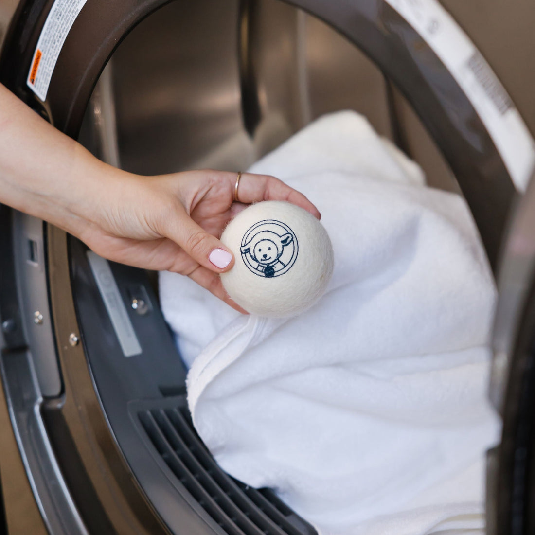 Hand placing Wool Dryerball into dryer with towels